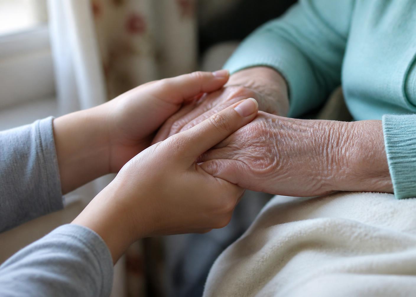 A caregiver sitting with a loved one beside a sunlit window with palm fronds outside